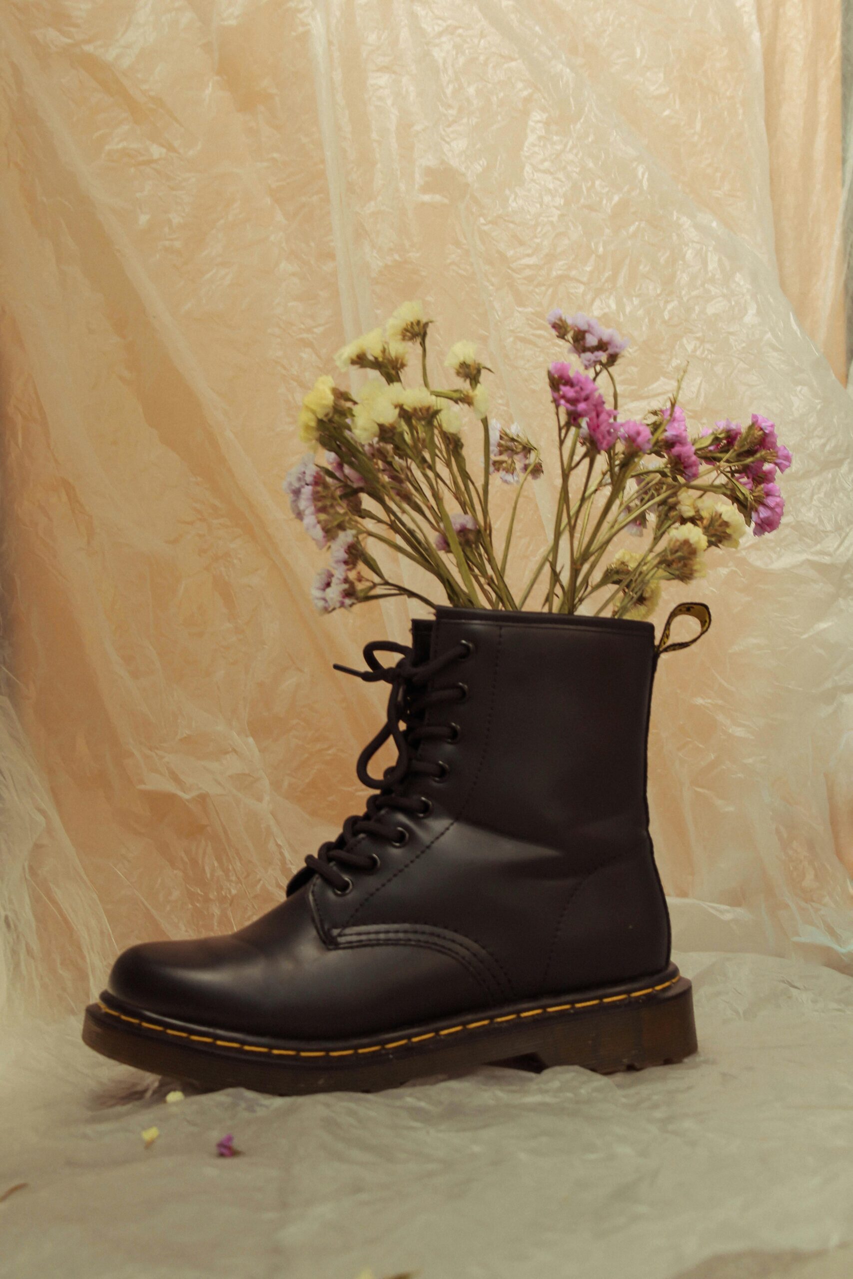 Black leather lace-up boots with flowers inside on a soft beige background