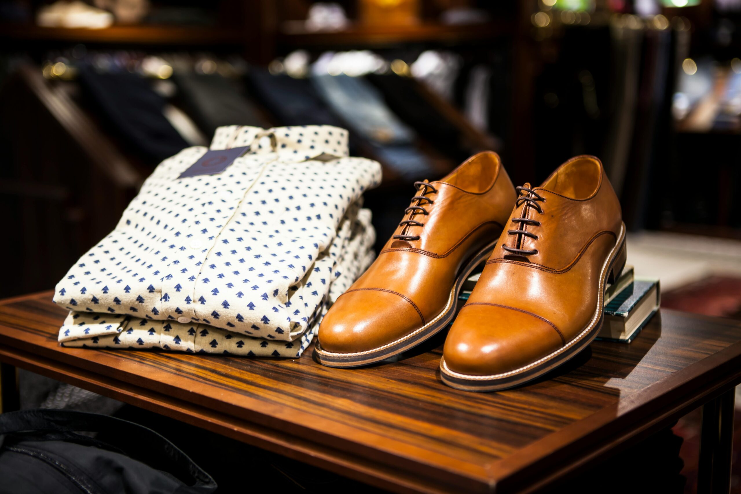 Brown leather dress shoes with folded patterned shirt on wooden display table